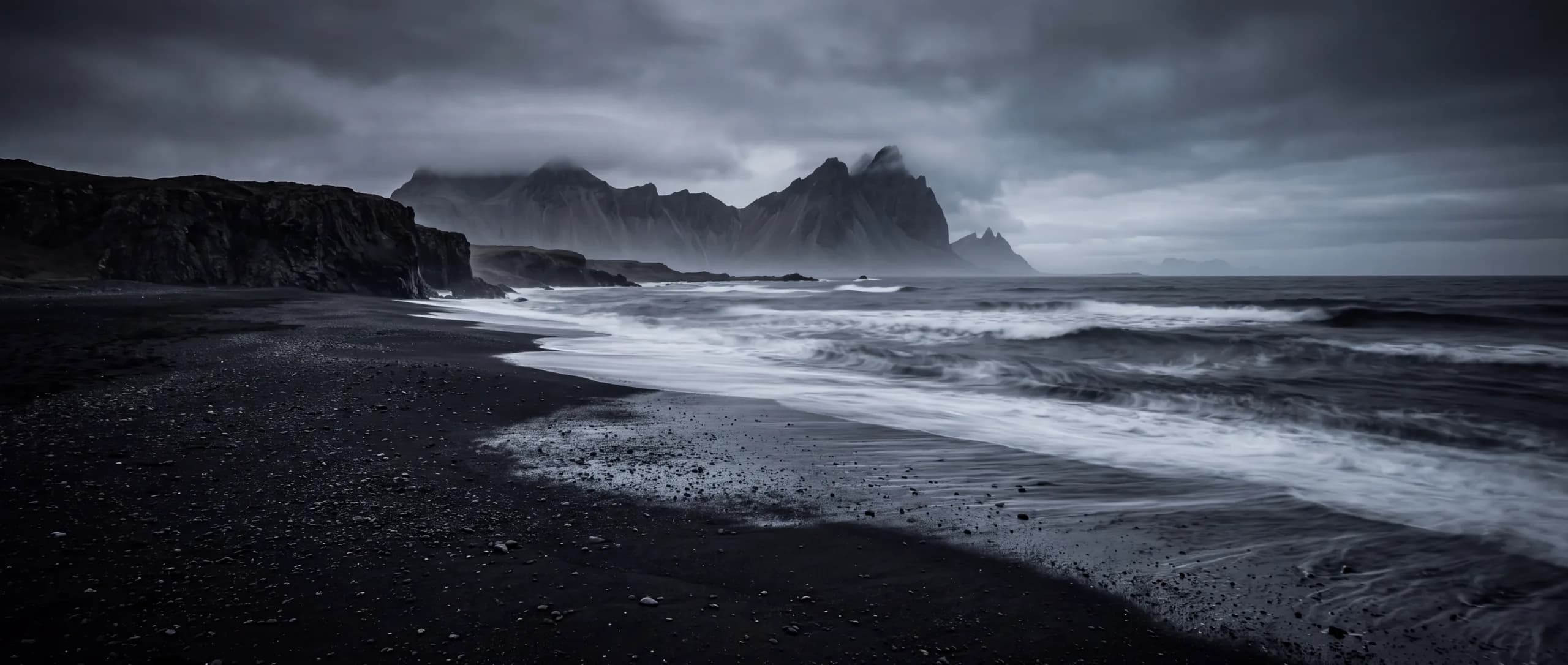 A black volcanic sand beach at dusk, mirror-still water reflecting a charcoal sky
